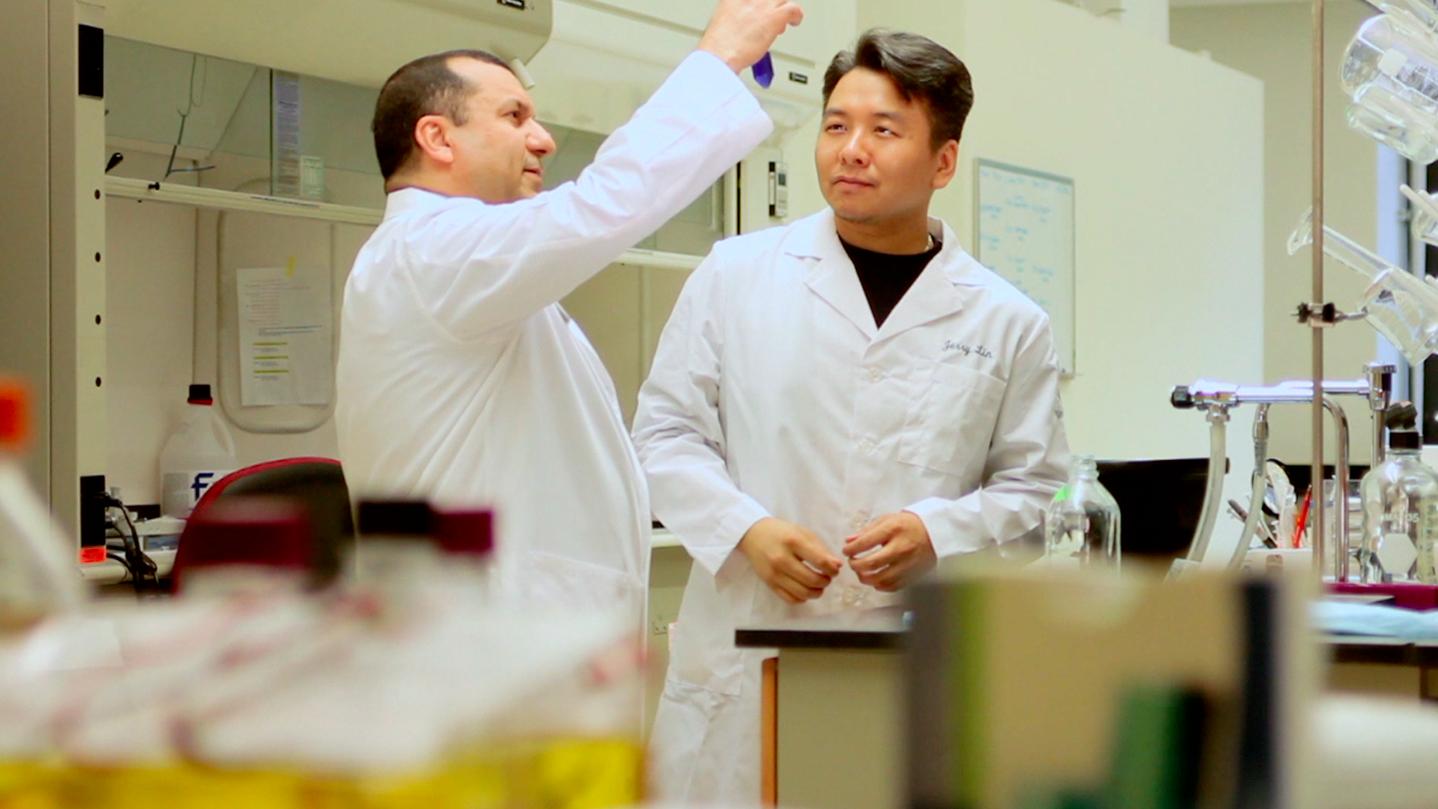 Two researchers in white coats examine a sample